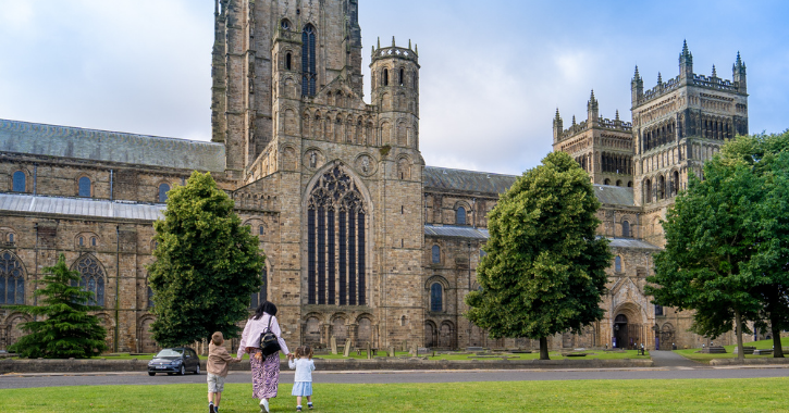 Family with children walking across Palace Green towards Durham Cathedral.